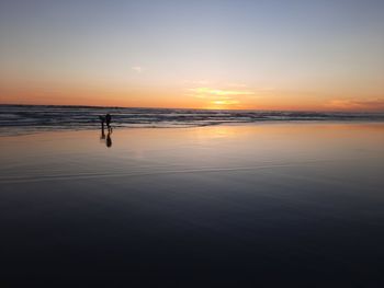 Lover couple walking on wet sand beach at sunset