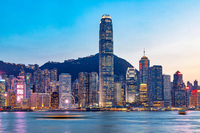 Sea by illuminated buildings against sky in city