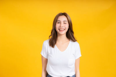 Portrait of smiling young woman against yellow background