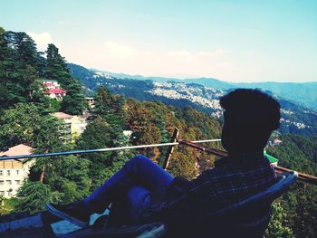 Rear view of woman sitting on mountain against sky