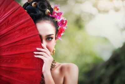 Close-up portrait of beautiful woman hiding behind red umbrella