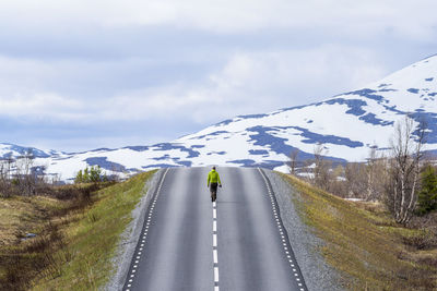 Rear view of man on snow covered road against sky