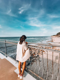 Rear view of woman standing on beach against sky