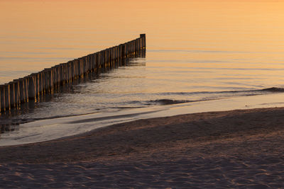 Wooden posts on beach against sky during sunset