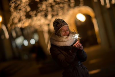 Smiling young woman holding sparkler at night