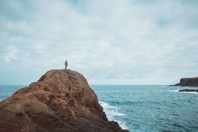 Rear view of woman standing on cliff by sea against cloudy sky