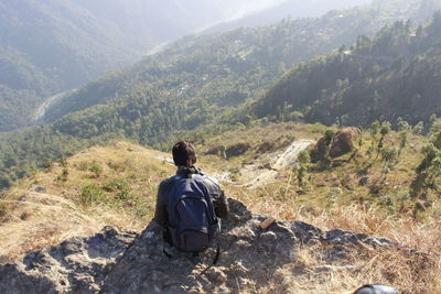 Rear view of man sitting on mountain against sky