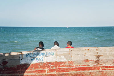 People on wall by sea against clear sky