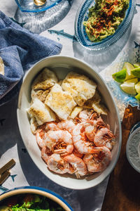 Seafood table spread to make fish tacos, prawns, guacamole, lime, tortilla, salsa on fish tablecloth