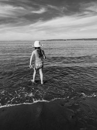 Rear view of woman standing on beach against sky