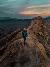 Rear view of man on mountain against sky during sunset