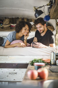 Smiling couple sharing smart phone while lying on bed in caravan