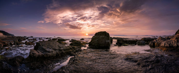 Panoramic view of rocky seashore against sky during sunset