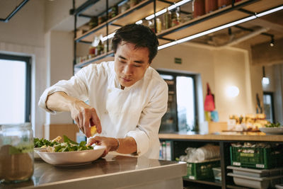 Male chef squeezing lemon on salad at kitchen counter in commercial kitchen