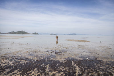 Woman collecting oysters on beach against sky