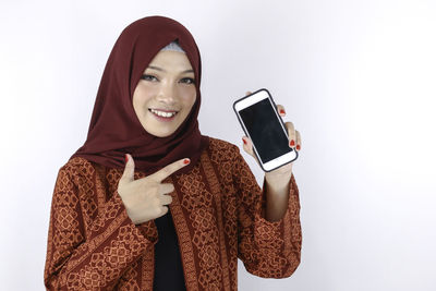 Portrait of smiling young woman using smart phone against white background