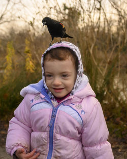 Cute girl with bird perching on head against plants