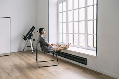 Young man looking through window sitting on chair at home