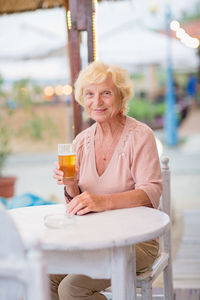 Mature woman sitting at a table in a summer cafe and drinking beer