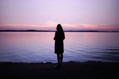 Silhouette woman standing at lakeshore during sunset