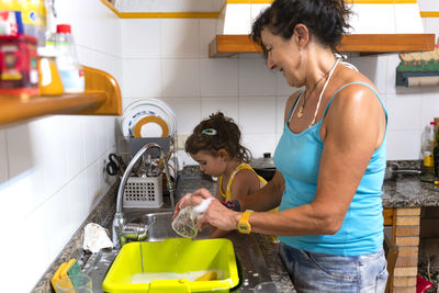 Little girl helping grandmother washing dishes in the kitchen at home