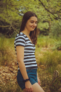 Side view of smiling young woman standing in forest