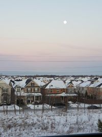 Snow covered houses against sky during sunset