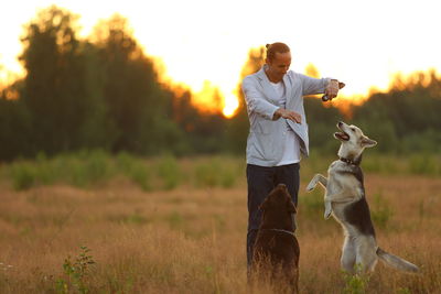 Man playing with dogs on grassy land during sunset