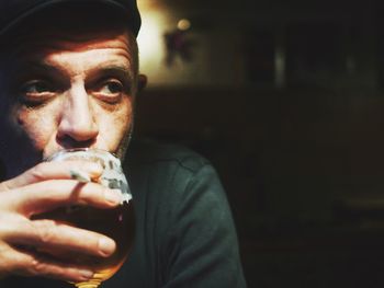 Close-up of man drinking beer while holding cigarette at home
