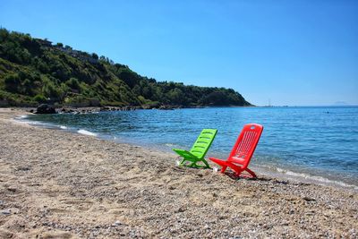 Deck chairs on beach against clear blue sky
