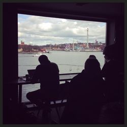 Rear view of silhouette men sitting on cityscape against sky