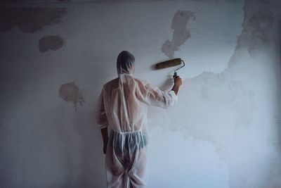 Rear view of man painting wall at home