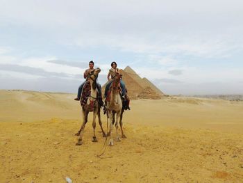 Man and woman enjoying camel ride against cloudy sky