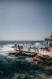 People at beach against clear sky during sunny day