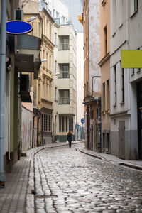Rear view of woman walking amidst buildings on alley in city
