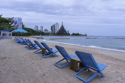 Empty chairs on beach against sky