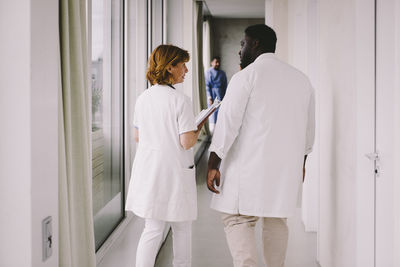 Senior female doctor discussing with male colleague while walking in corridor at hospital