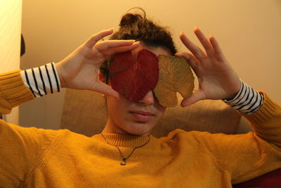 Young woman covering eyes with leaf decorations at home