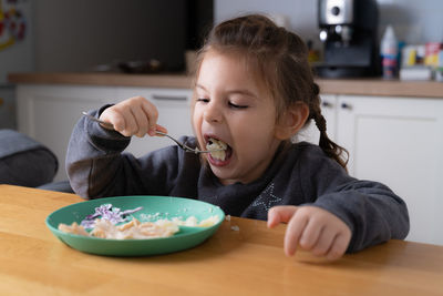 Little child girl sitting at the table and putting spoon at her mouth 