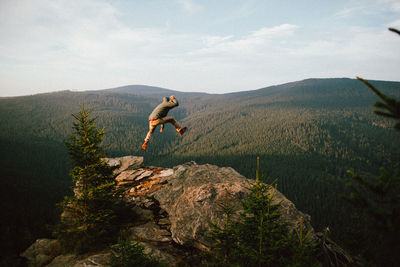 Rear view of man jumping on mountain against sky