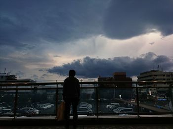 Rear view of man standing in city against cloudy sky