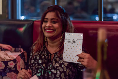 Smiling woman holding greeting card at table