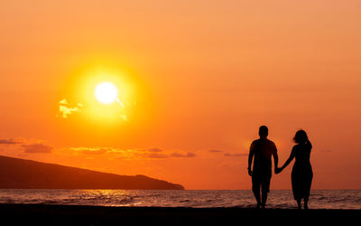 Couple holding hands at beach, silhouette in sunset, love and friendship.