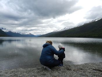 Mother and son at lakeshore against cloudy sky