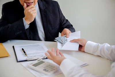 Cropped hands of man giving money in envelope to businessman