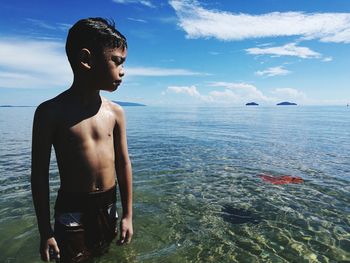 Shirtless boy standing in sea against sky