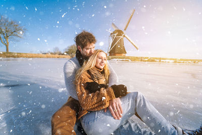 Happy couple embracing while sitting on frozen lake