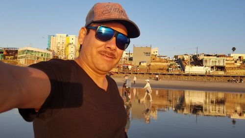 Portrait of man wearing sunglasses at beach against clear blue sky
