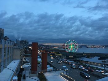 Illuminated ferris wheel in city against sky