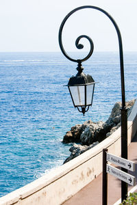 View of lamp post by sea against clear sky